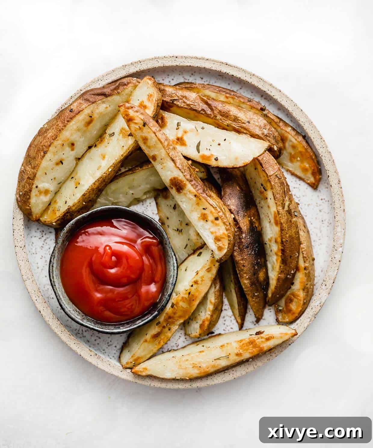 Crispy Baked Potato Wedges on a plate with a black bowl filled with ketchup.