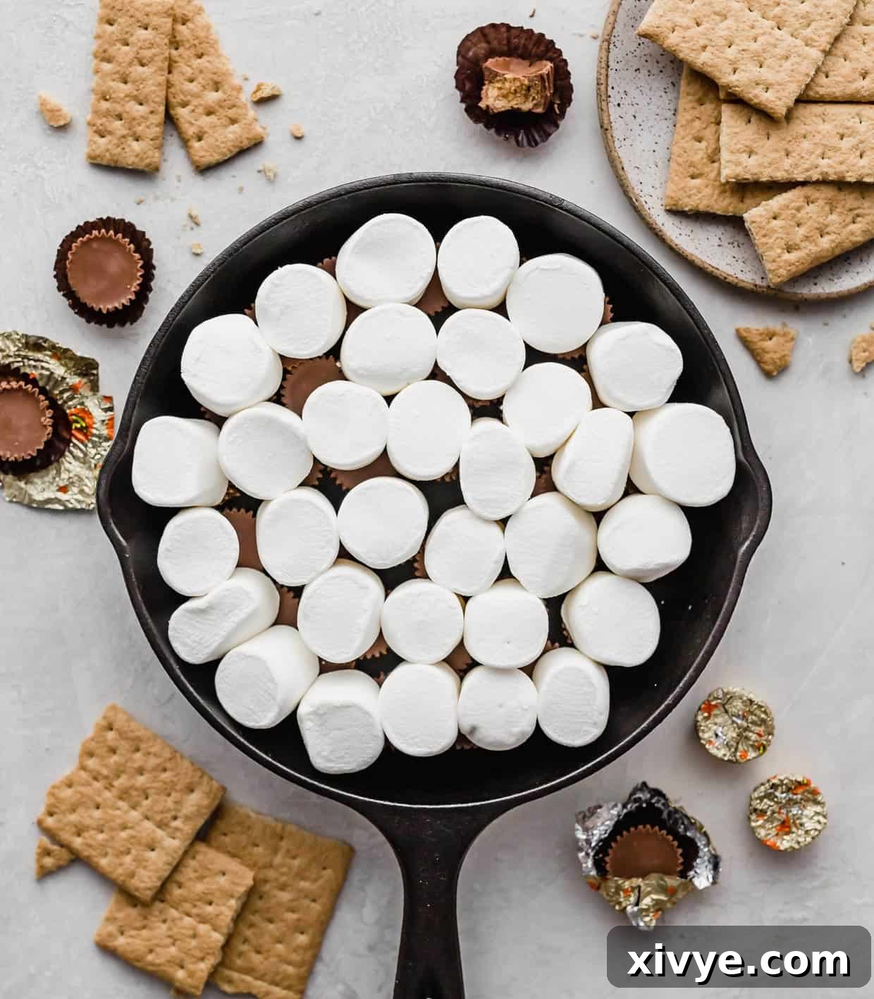 Large marshmallows overtop of Reese's peanut butter cups in a black skillet.
