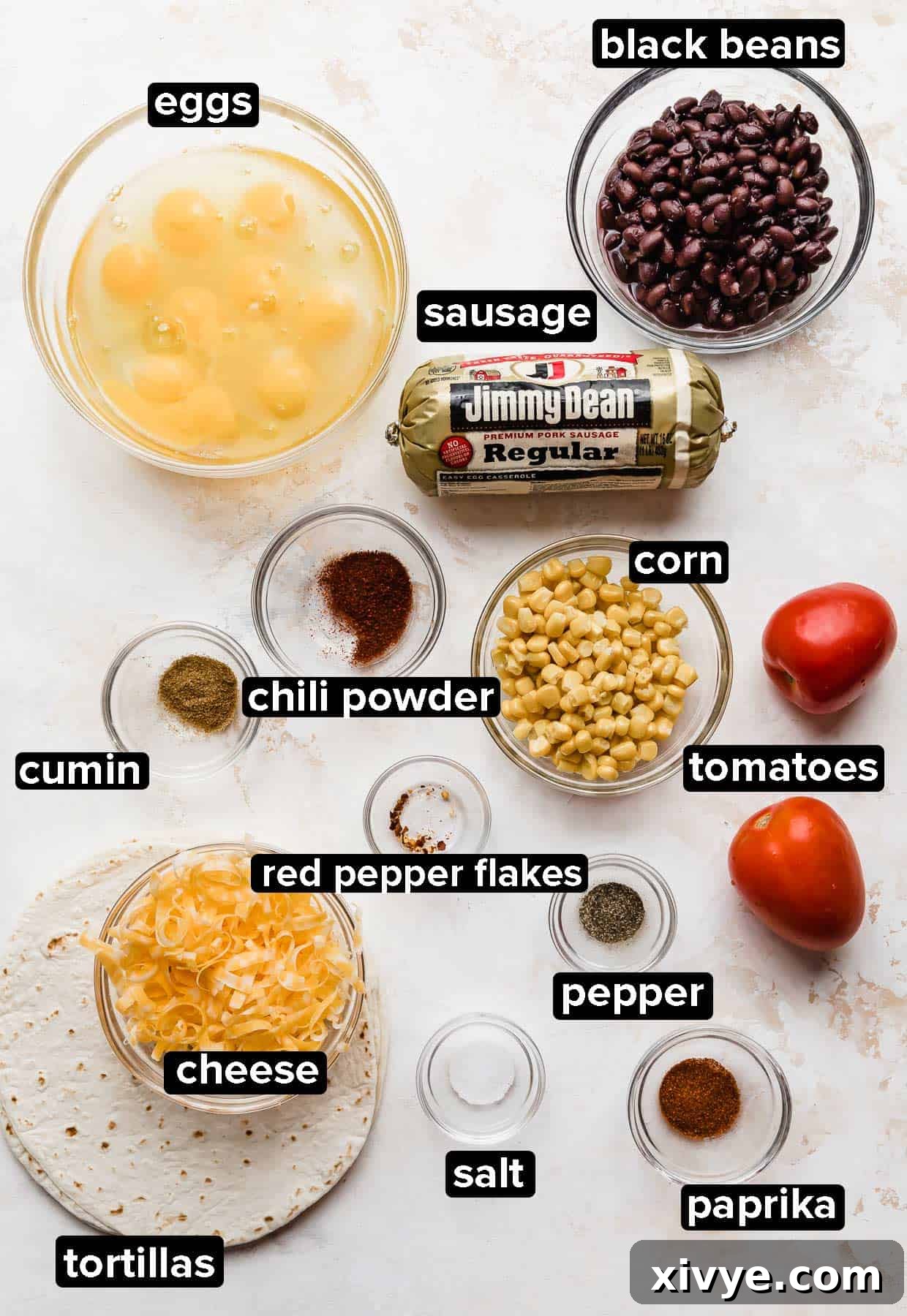 Ingredients used to make Breakfast Burrito with Black Beans and egg and sausage, portioned into glass bowls on a white textured background.