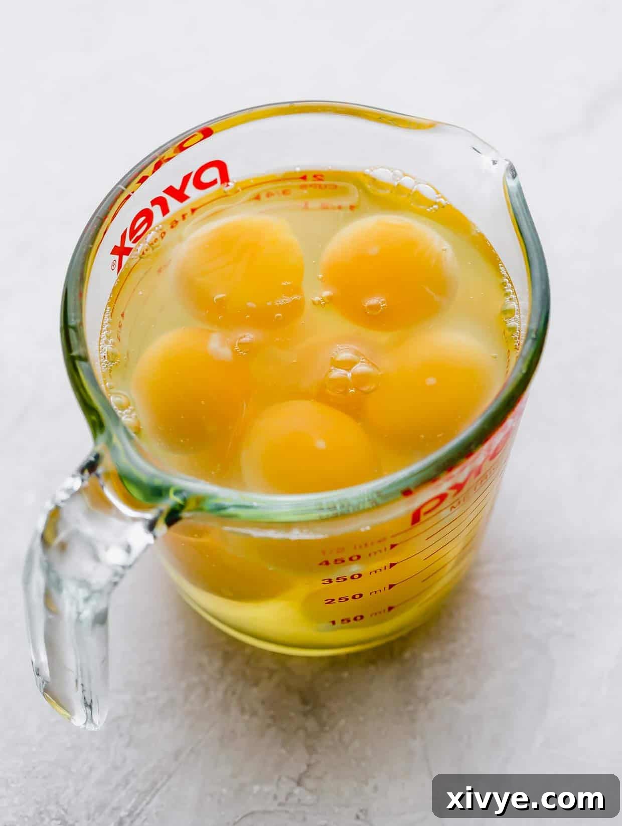 A glass liquid measuring cup with cracked eggs in it.
