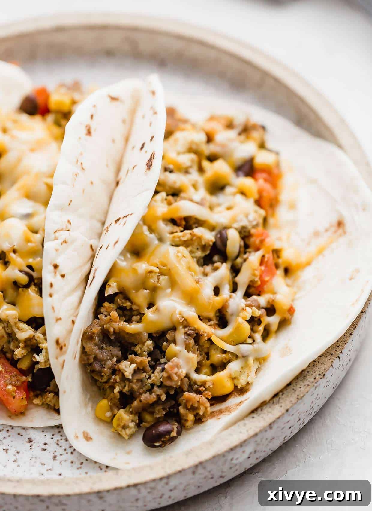 A tortilla filled with a sausage, egg, black bean mixture and topped with melted orange cheese.