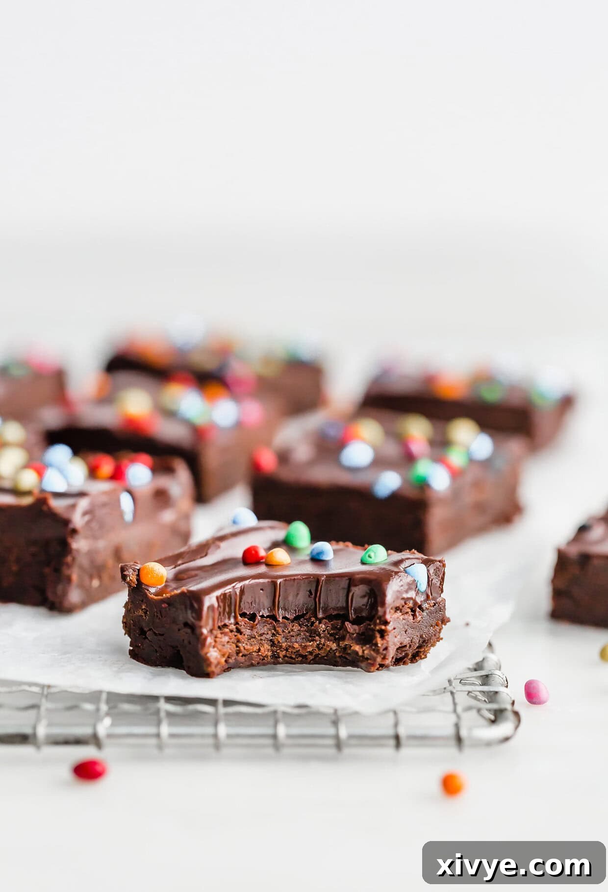 Cosmic Brownie Magic 2 Homemade cosmic brownies topped with colored cosmic sprinkles, one brownie having a bite taken out of it, against a white background.