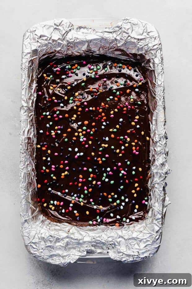 Cosmic Brownie Magic 13 Rainbow chip topped Cosmic Brownies in a baking dish, glistening with ganache and colorful candies.