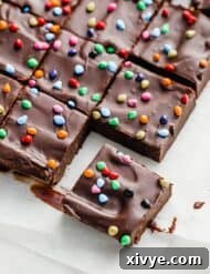 Squares of rainbow chip topped cosmic brownies on a white parchment paper.