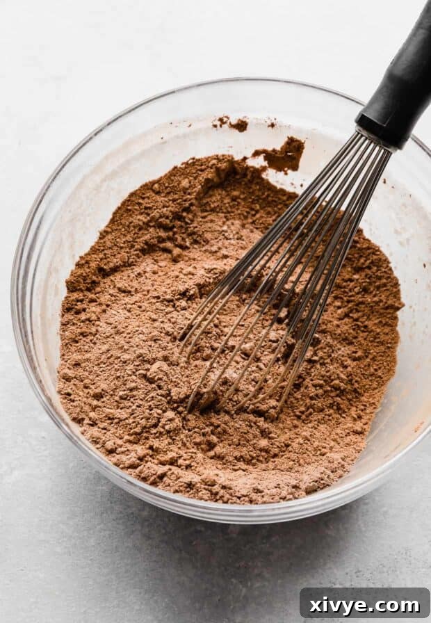 Cosmic Brownie Magic 6 A light brown colored dry ingredients in a glass bowl with a whisk mixing it together, showing flour, cocoa, cornstarch, and salt.