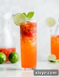 A tall mojito glass filled with a strawberry mojito mocktail with a lime wedge on the rim.
