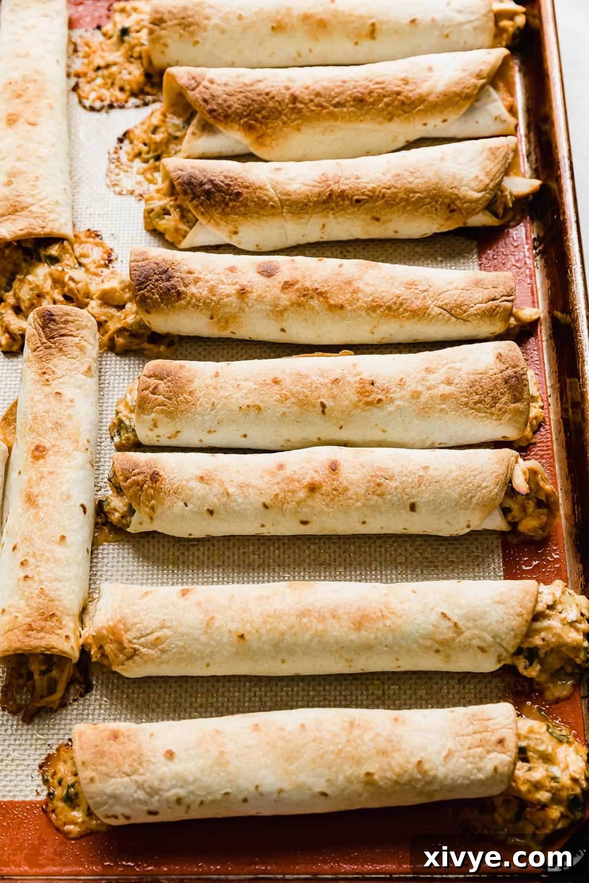 Golden brown baked chicken taquitos lined up on a baking sheet, fresh out of the oven.