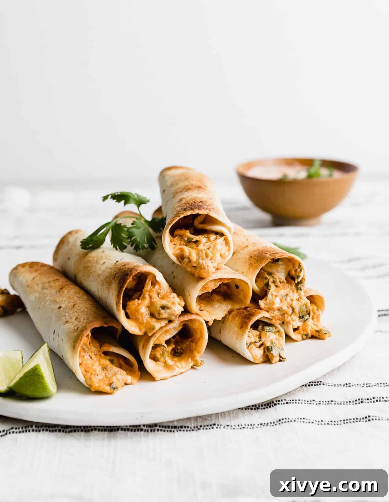 Baked Chicken Taquitos stacked on top of one another on a white plate, ready for serving.