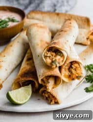 Baked Chicken Taquitos stacked on top of one another on a white plate with fresh parsley in the background.