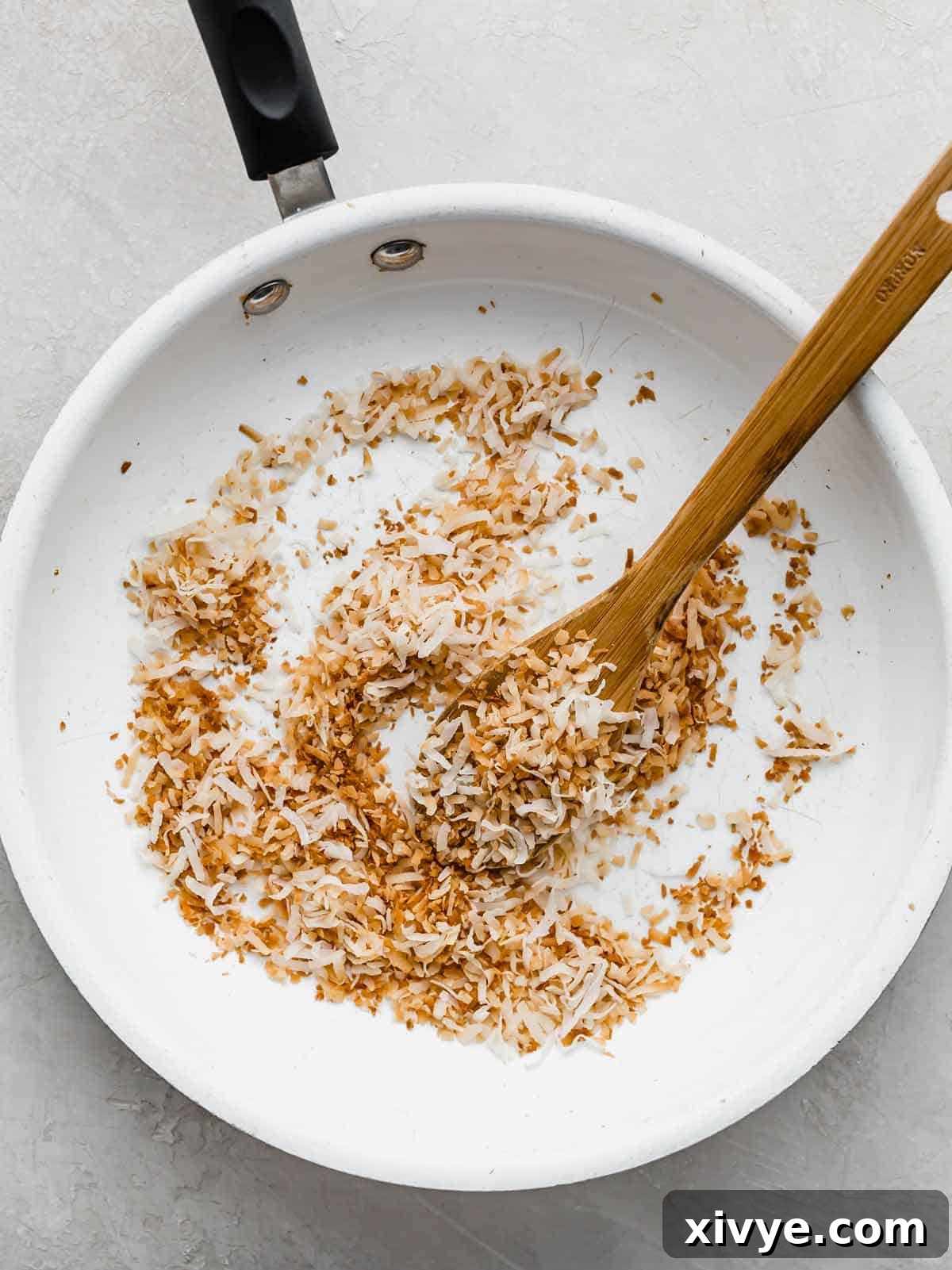 A white skillet containing perfectly brown toasted coconut, illustrating the stovetop method.