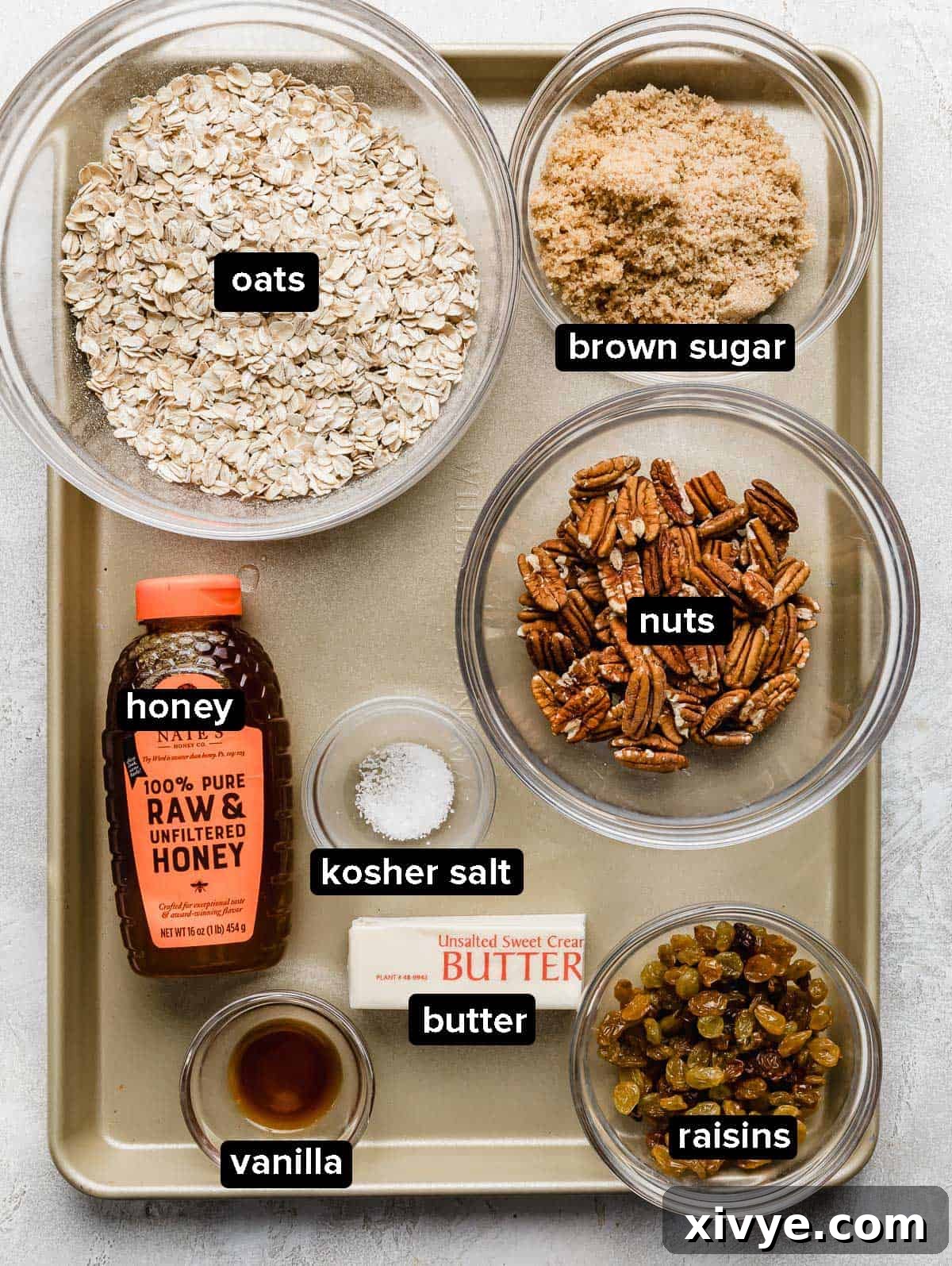 Wholesome Oat & Raisin Granola Bars 3 Homemade granola bar ingredients in glass bowls on a bronze colored baking sheet.