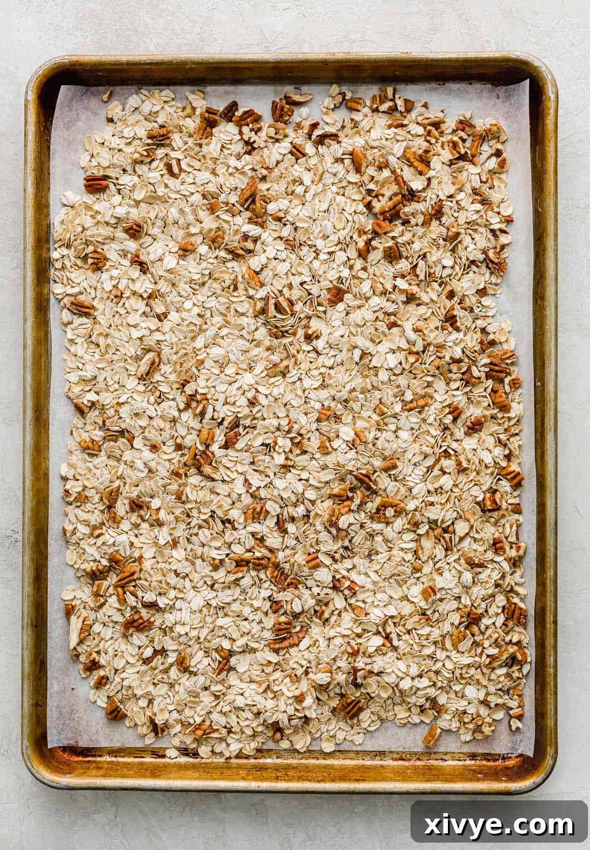 Wholesome Oat & Raisin Granola Bars 4 A baking sheet with old fashioned oats and chopped pecans spread across the surface of it.