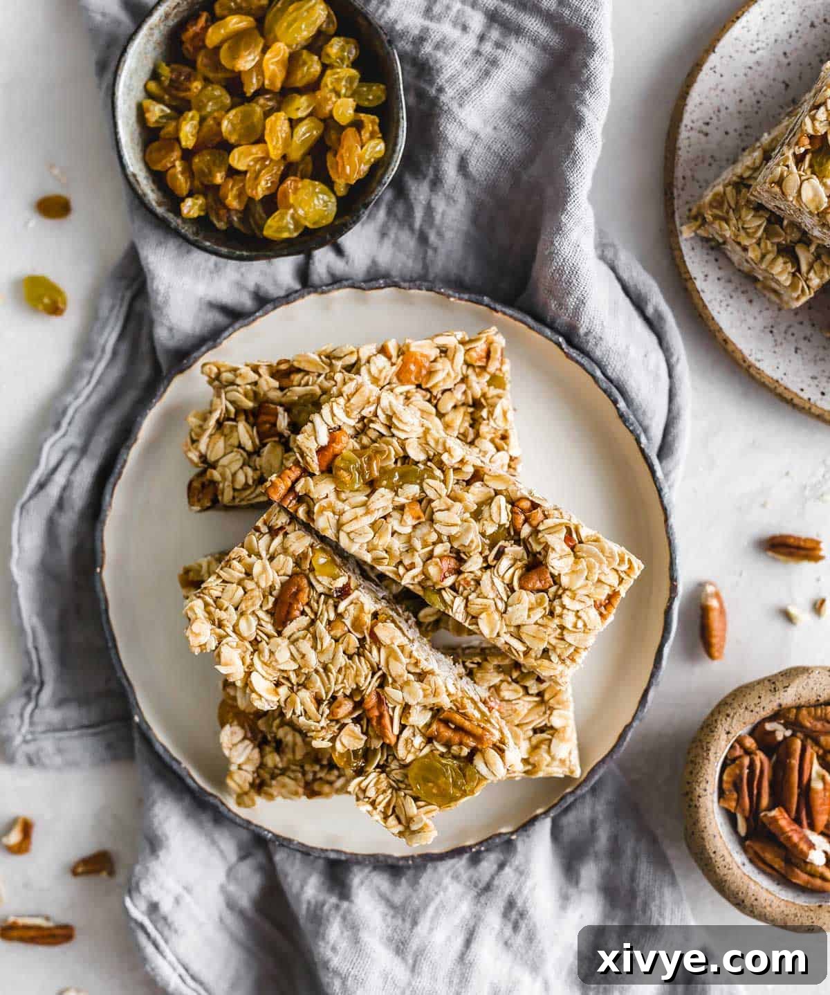 Wholesome Oat & Raisin Granola Bars 9 Homemade Oatmeal Raisin Granola Bars with nuts and golden raisins on a black rimmed white plate on a light gray linen napkin.