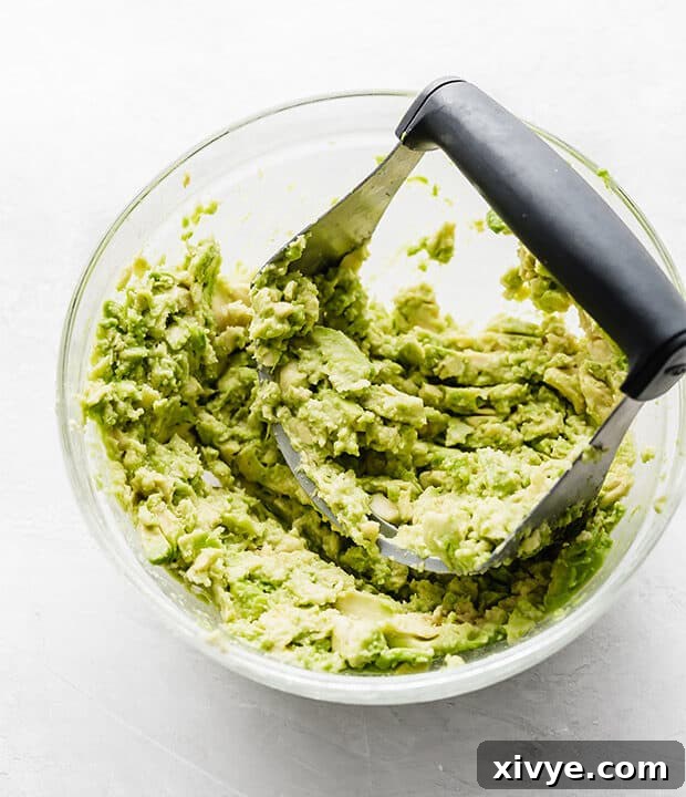 Creamy Avocado Chicken Wraps 5 A glass bowl with a pastry cutter mashing ripe avocados.