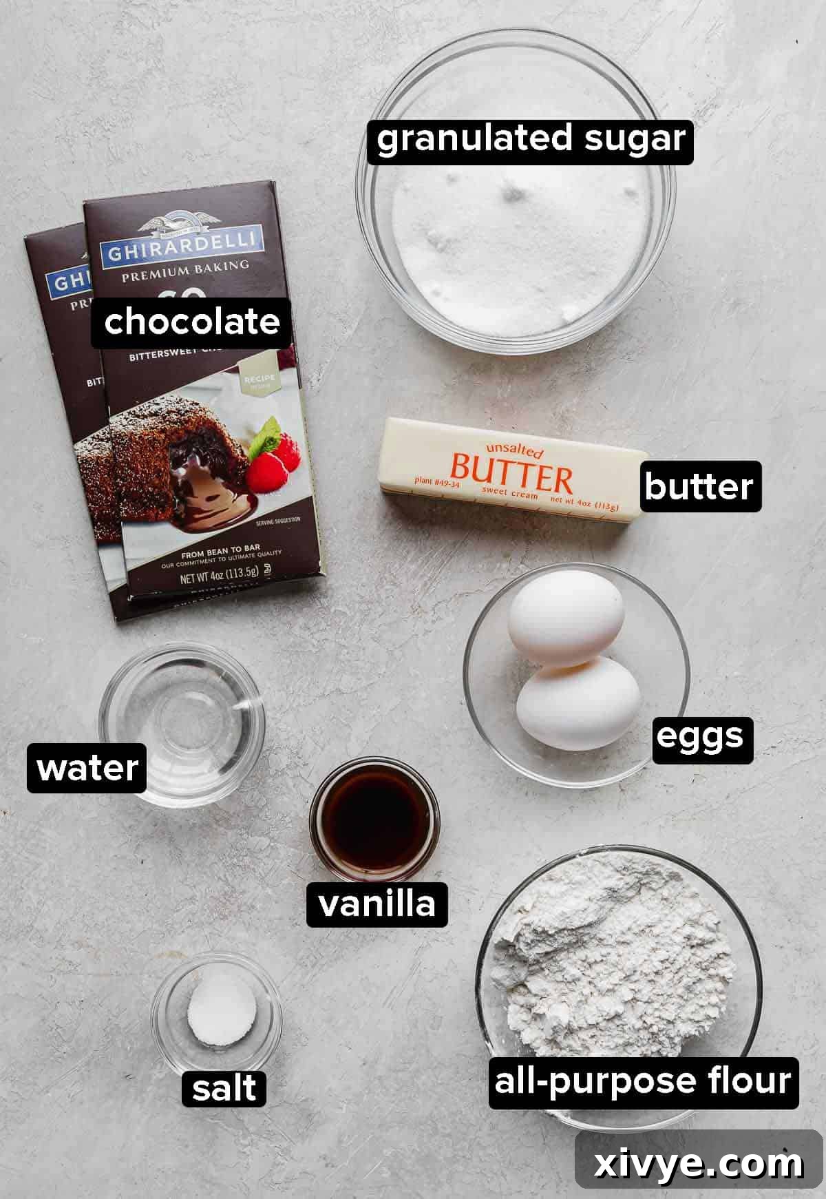 German Chocolate Brownie ingredients: sugar, eggs, butter, flour, vanilla, water, and chocolate bar, on a gray background.