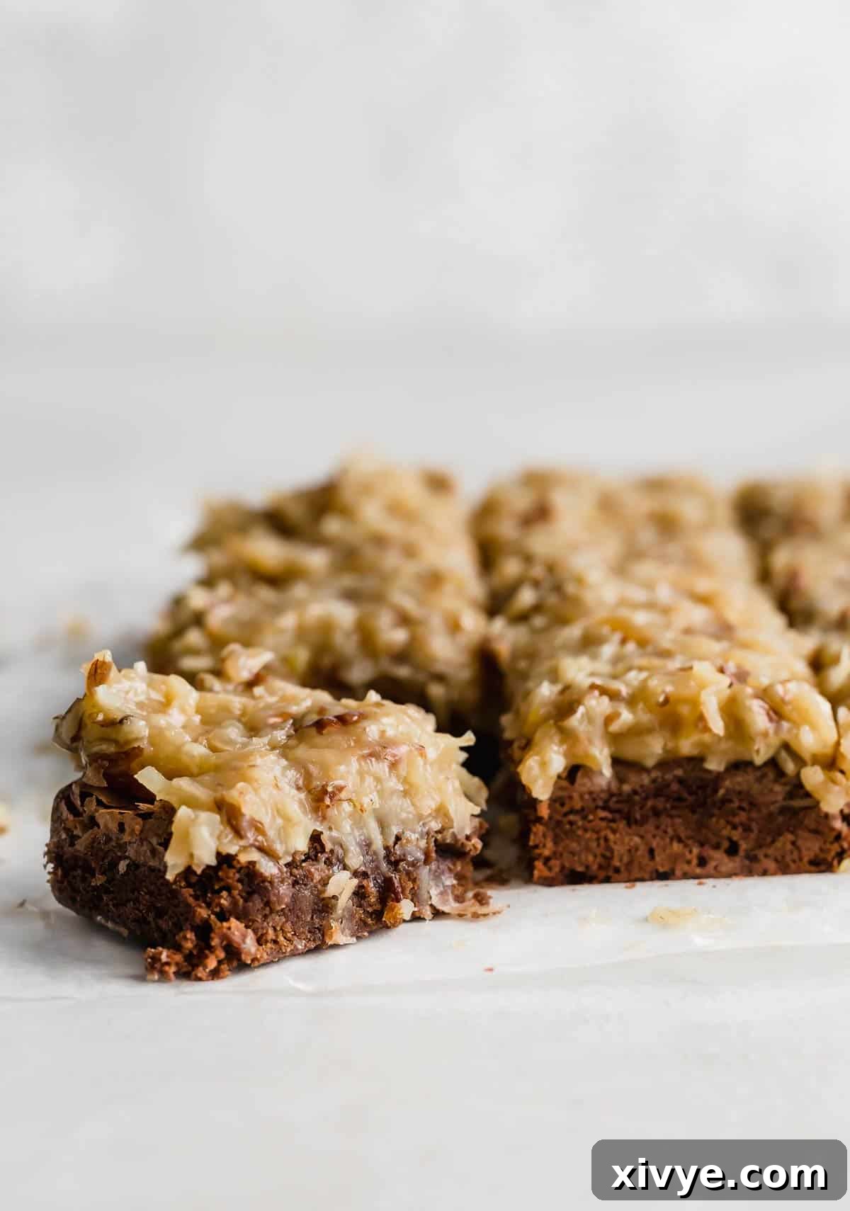 A square of German Chocolate Brownies topped with coconut pecan frosting against a white background. 