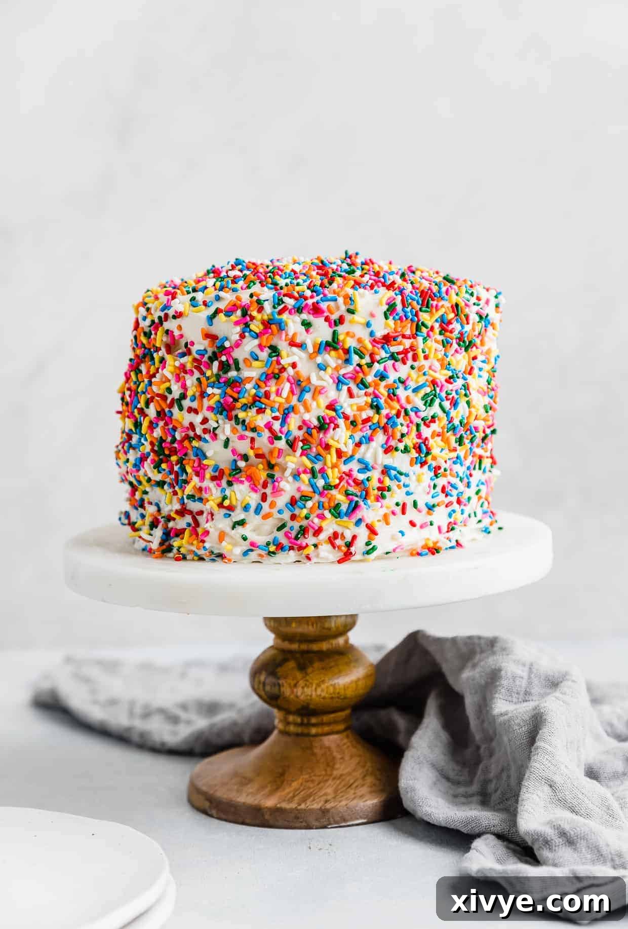 A beautifully decorated sprinkle smash cake recipe on a elegant cake stand, set against a clean white background, ready for a special celebration.