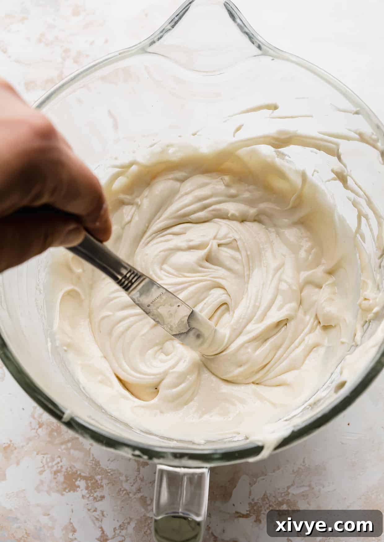 A butter knife gracefully slicing through a generous bowl of smooth, pale vanilla cake batter, preparing it for baking.