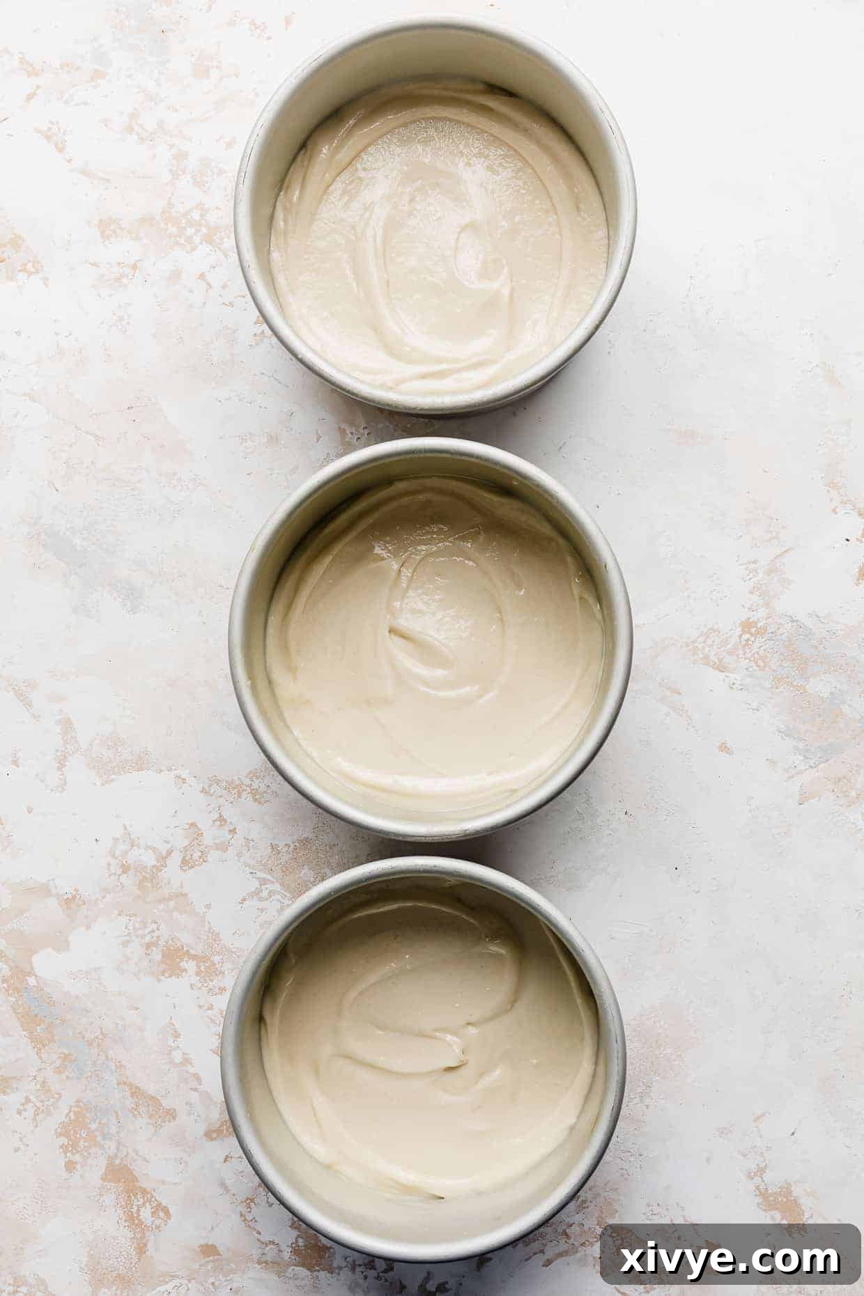 Three perfectly portioned vanilla cake batters in circular pans, lined up and ready to be baked to golden perfection.