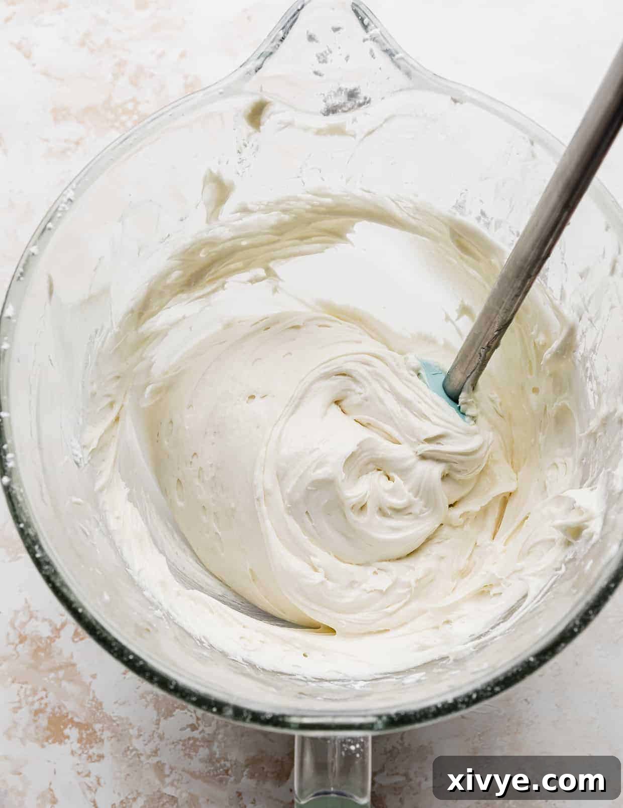 A generous amount of creamy vanilla cake frosting, whipped to perfection, resting in a glass mixing bowl, ready for application.