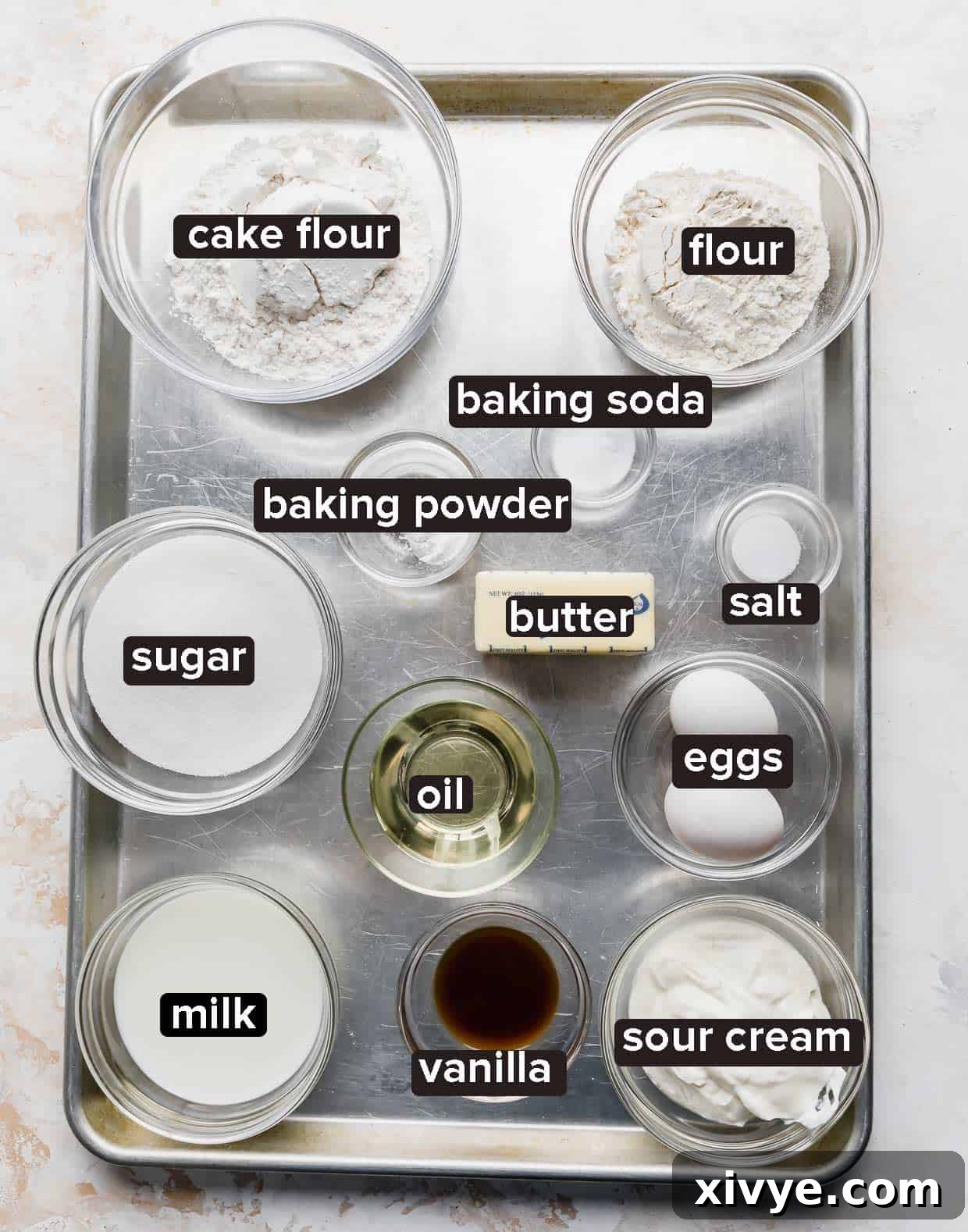 All the necessary ingredients for a delicious Smash Cake Recipe are neatly arranged on a shining silver baking sheet, ready for preparation.