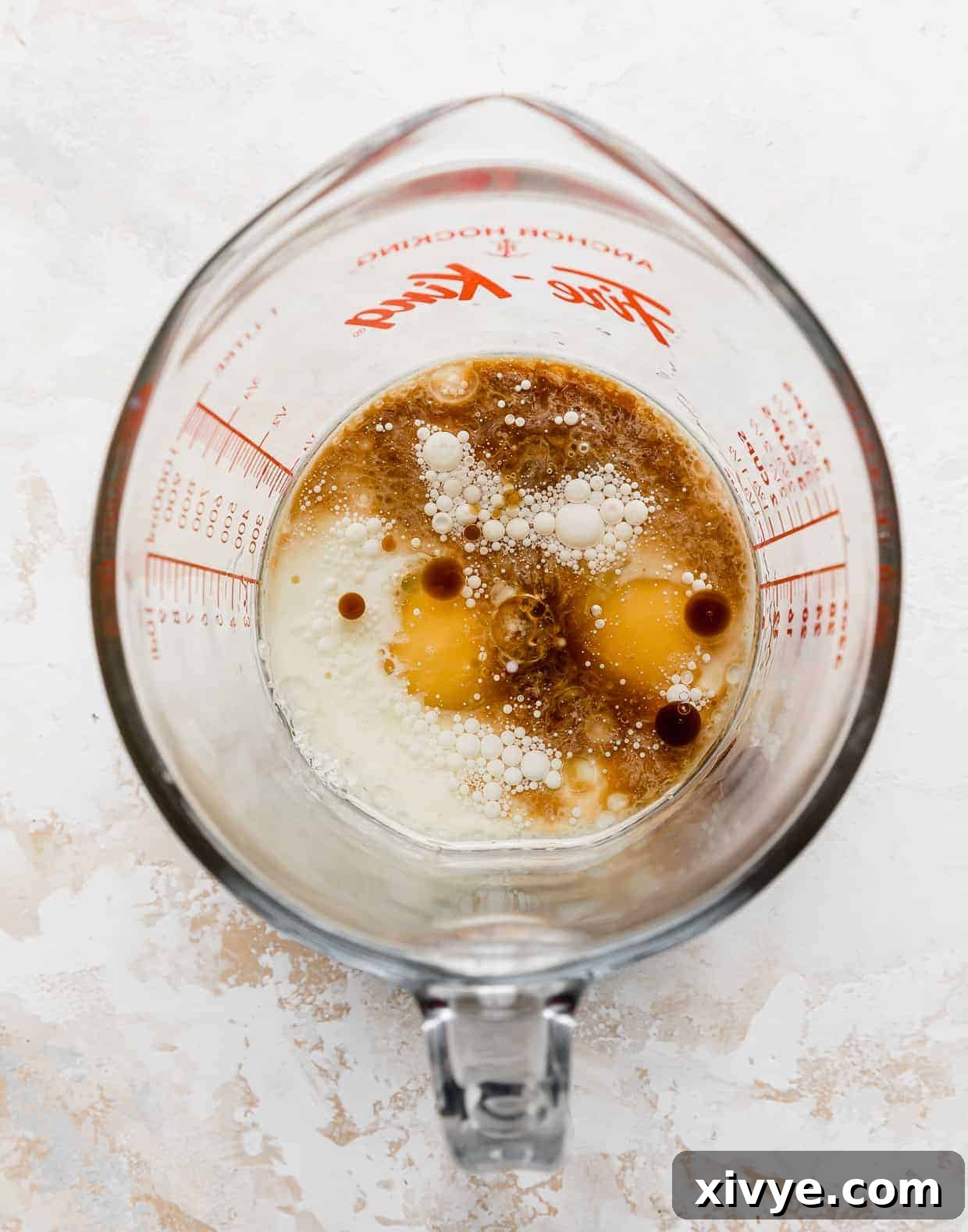 A liquid measuring cup holding a mixture of eggs, vanilla, and buttermilk, ready to be incorporated into the cake batter.