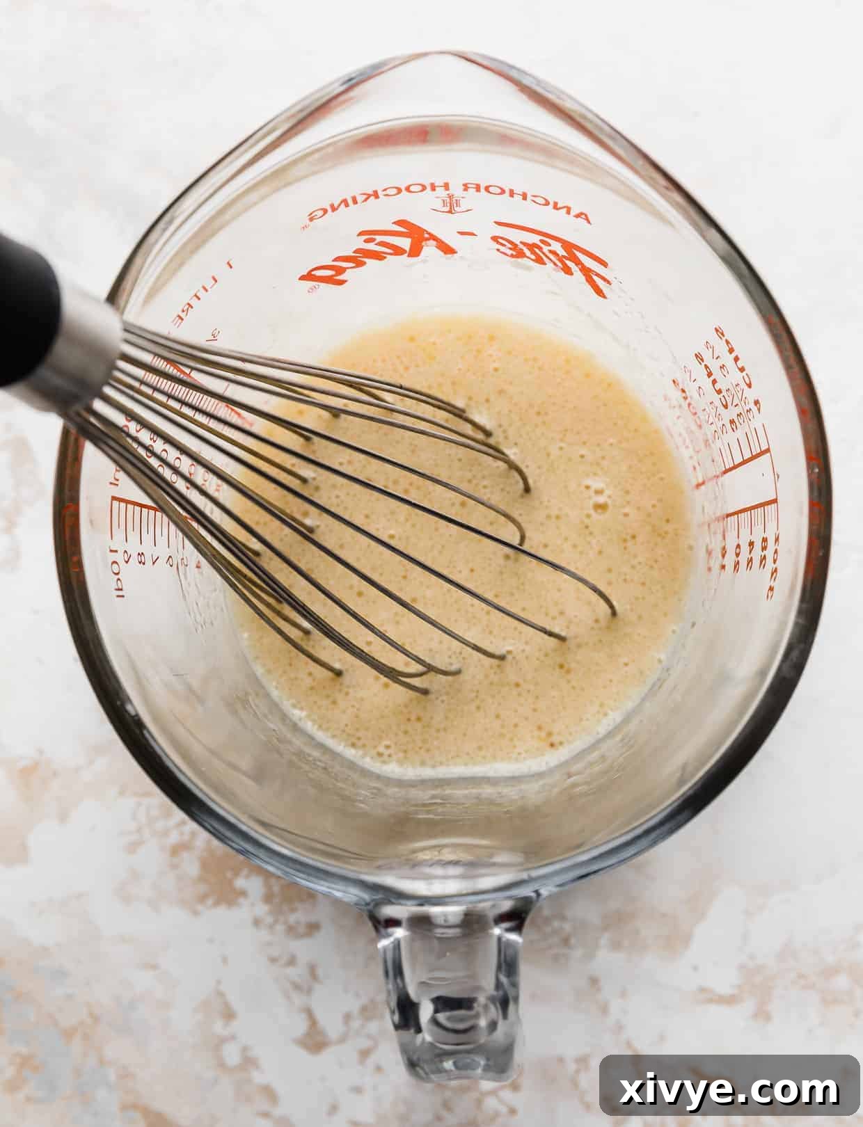 A measuring cup filled with a smooth, golden yellow liquid mixture, indicating thoroughly combined wet ingredients for the cake.