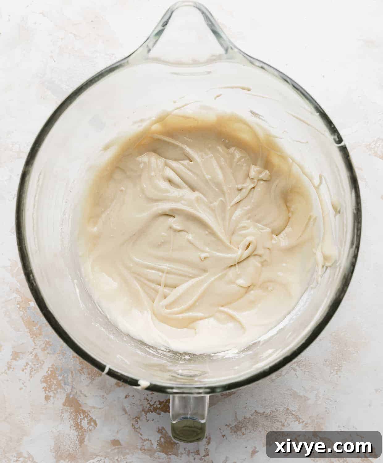 An inviting off-white colored vanilla cake batter, beautifully smooth and ready for baking, resting in a clear glass mixing bowl.