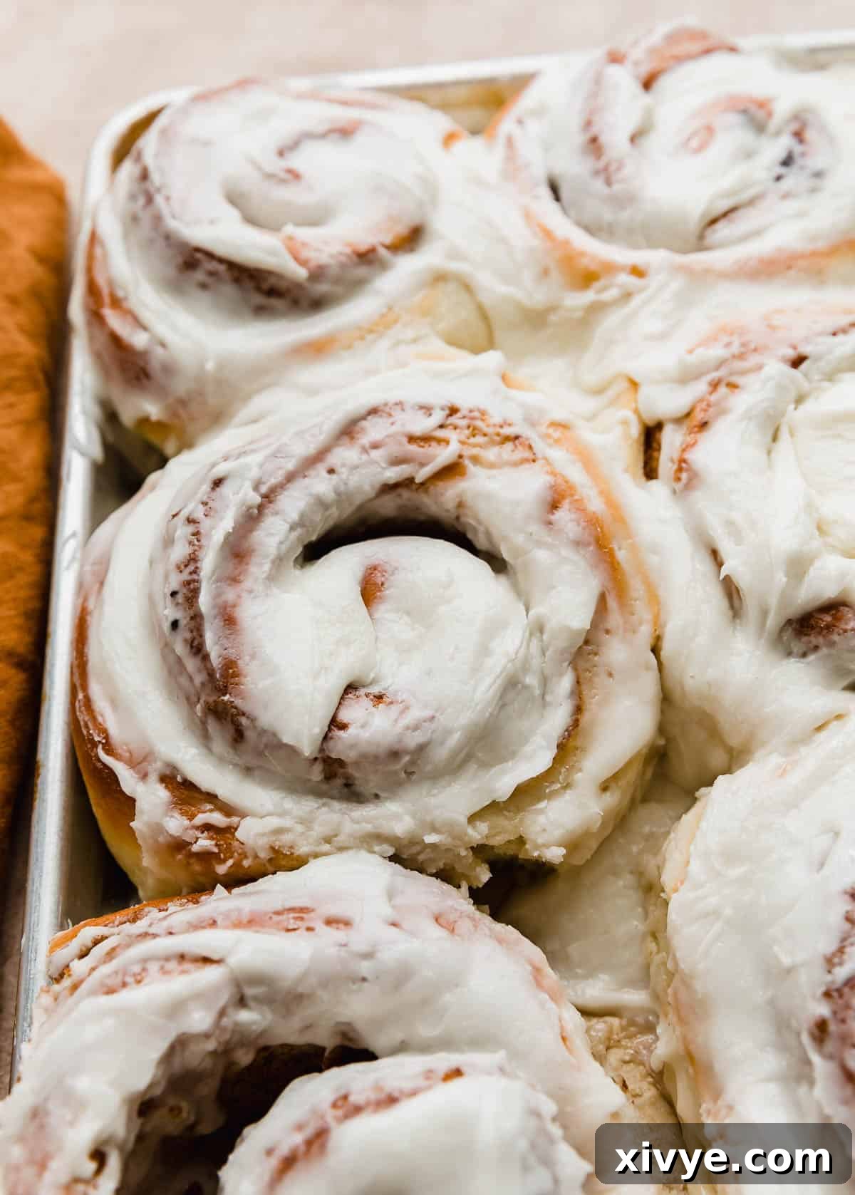 Large cinnamon roll covered in white frosting on a baking sheet.