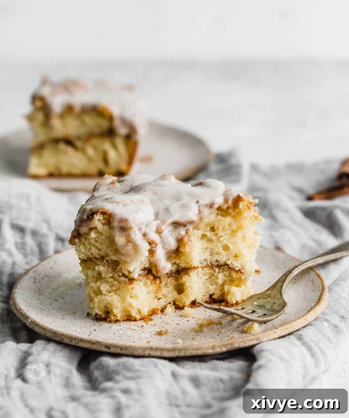 A slice of Cinnamon Roll Cake topped with glaze on a plate, showcasing its moist texture and cinnamon swirls.