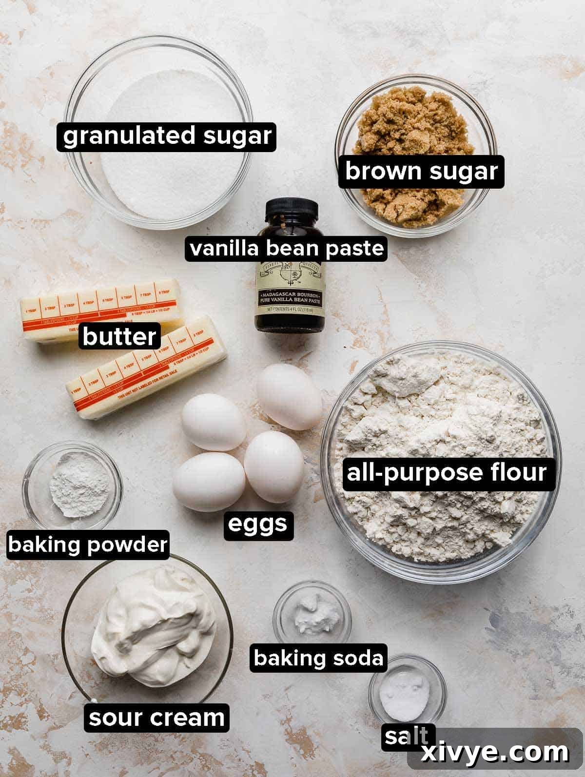 Cinnamon Roll Cake ingredients portioned into glass bowls on a white textured background.