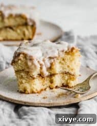 A glazed cinnamon roll cake slice on a tan colored plate.