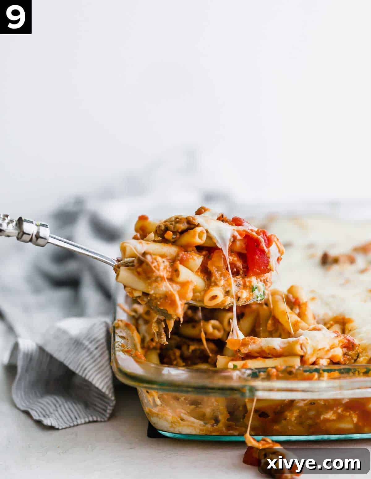 Comforting Sausage Ziti Bake 6 A spoon scooping up baked ziti from a casserole dish, showing gooey cheese and rich sauce.