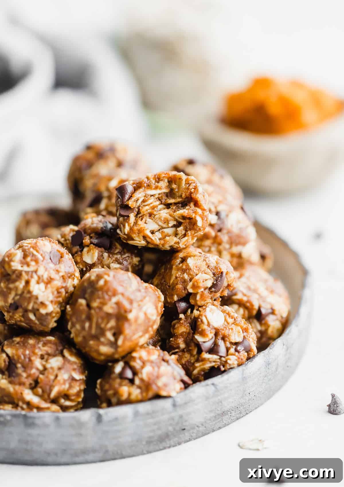 A beautifully composed shot of several pumpkin energy balls stacked on a white plate, with a rustic pumpkin puree backdrop.