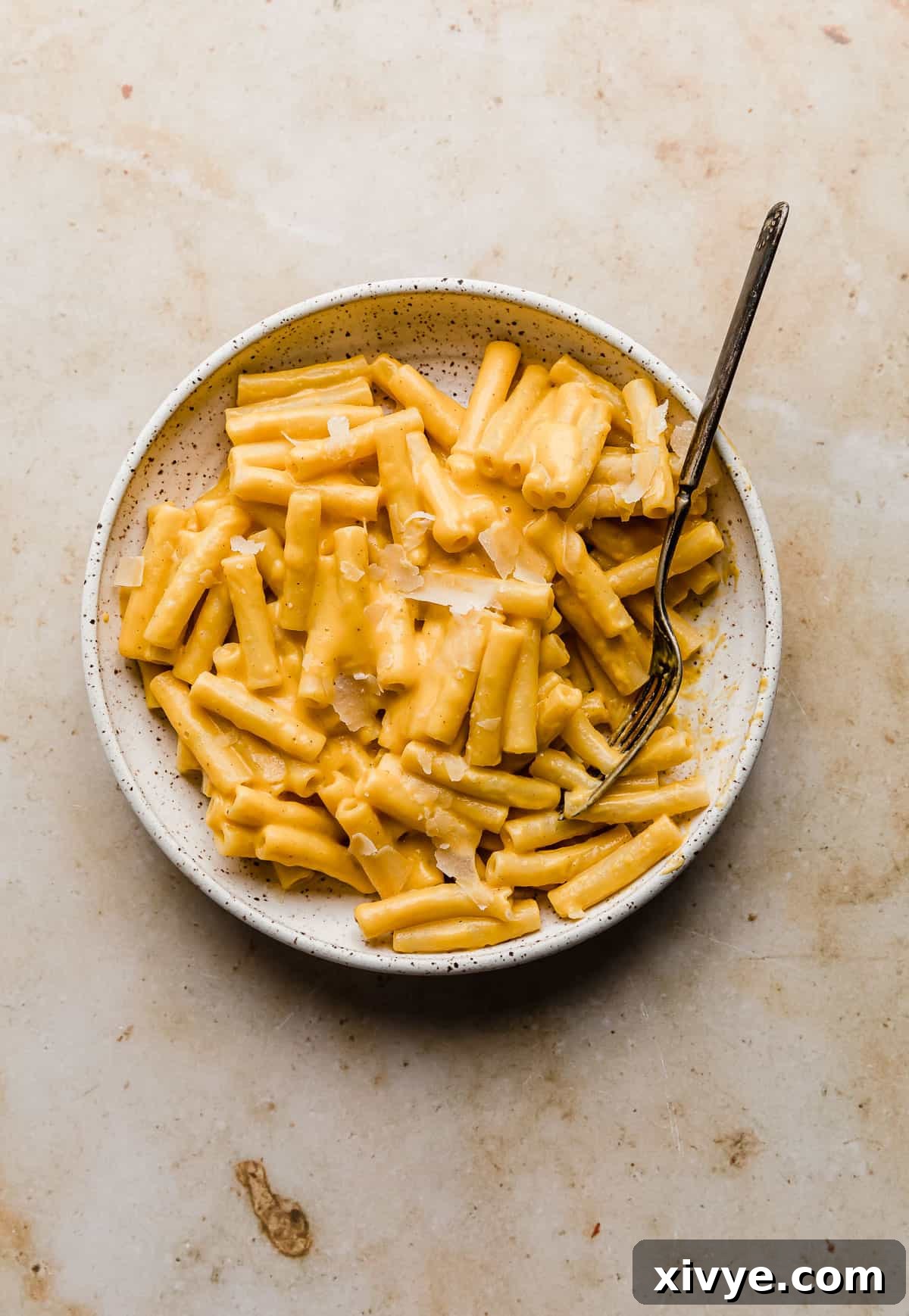 A beautifully plated dish of creamy roasted butternut squash pasta, garnished and ready to be served on a pristine white plate against a warm tan marble backdrop.