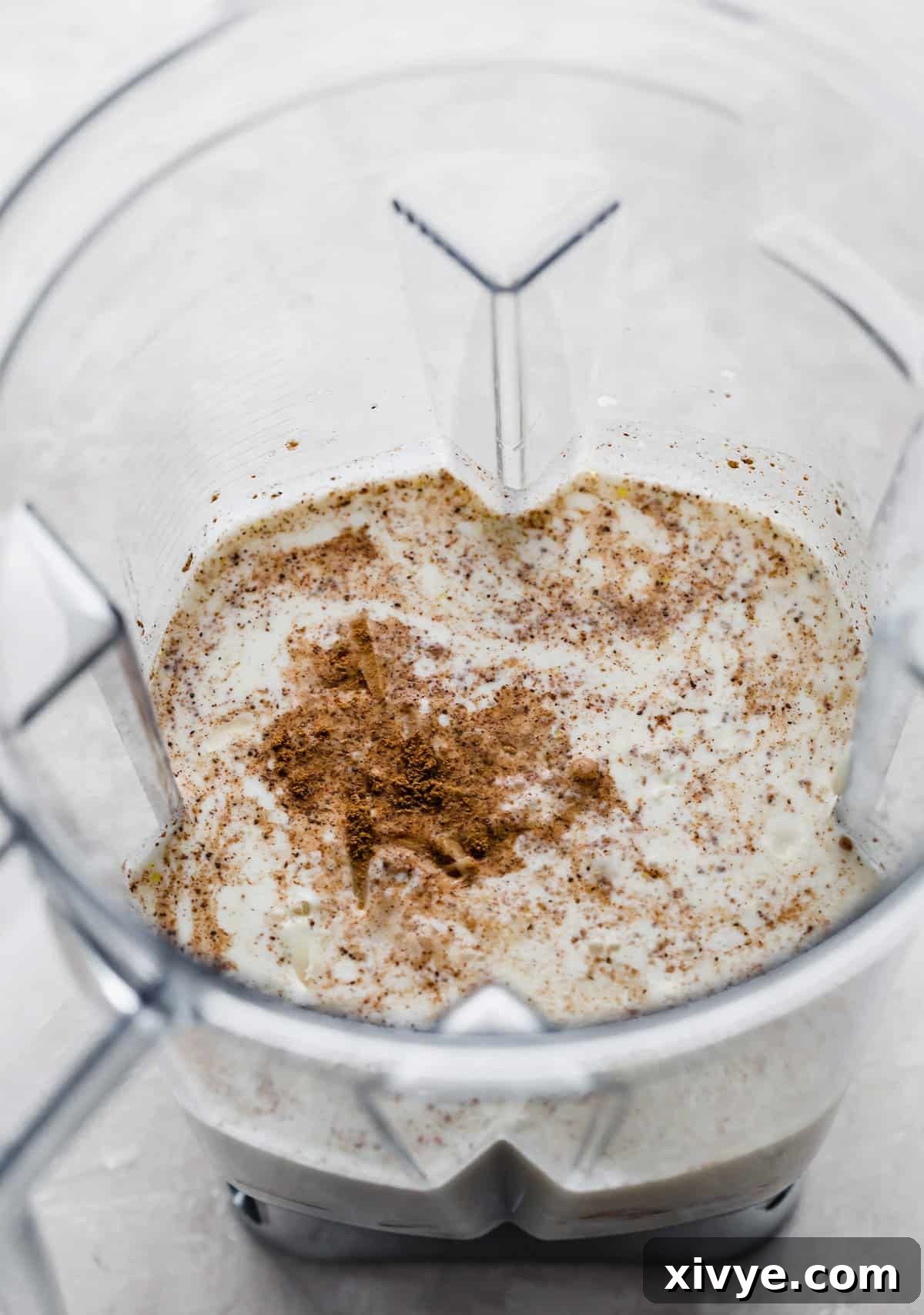 A blender filled with rich half and half, elegantly topped with a dusting of freshly ground nutmeg, ready to be blended into the butternut squash pasta sauce.
