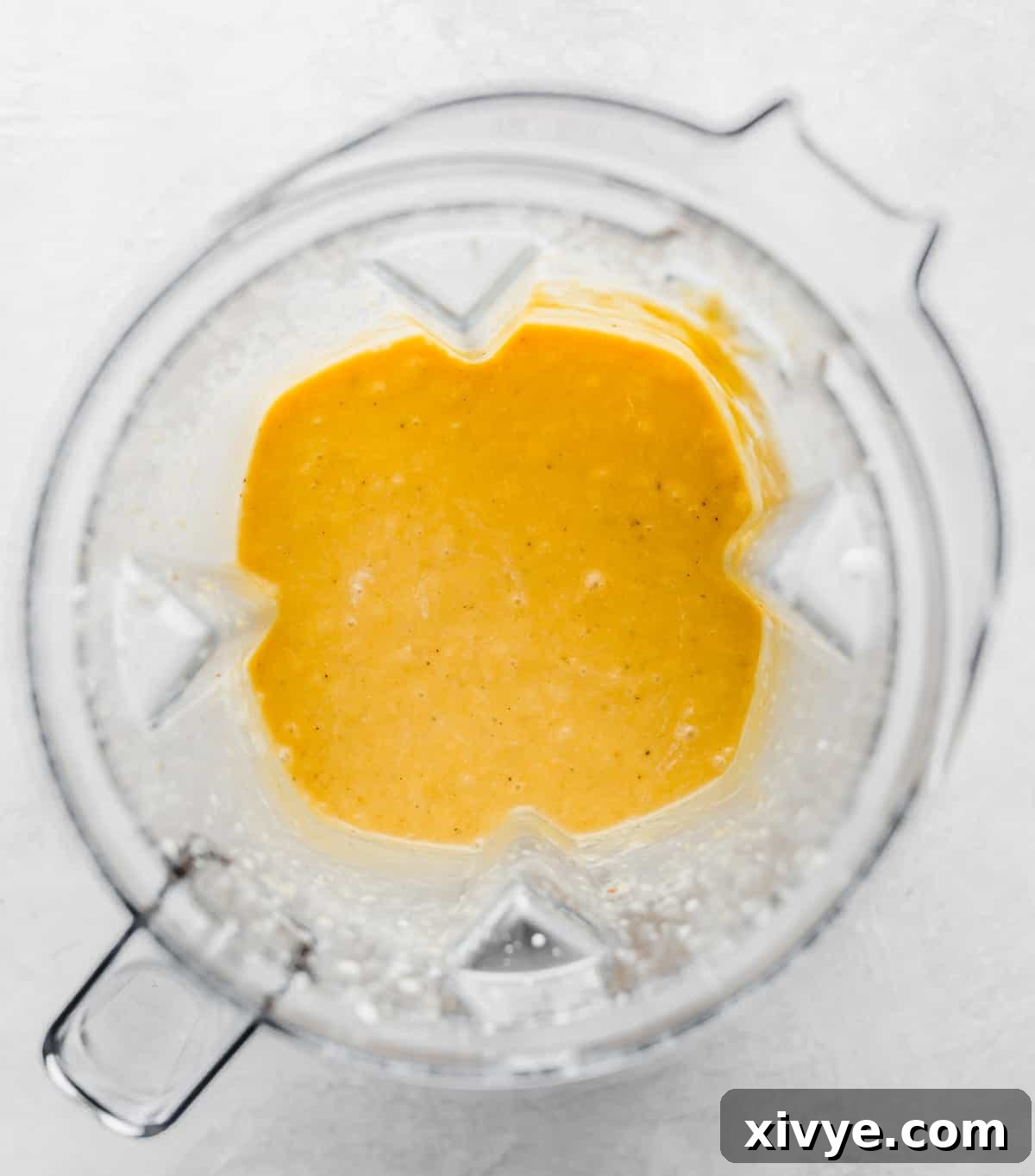 A blender holding a vibrant, pureed roasted butternut squash pasta sauce, showcasing its smooth and creamy texture against a clean white background.