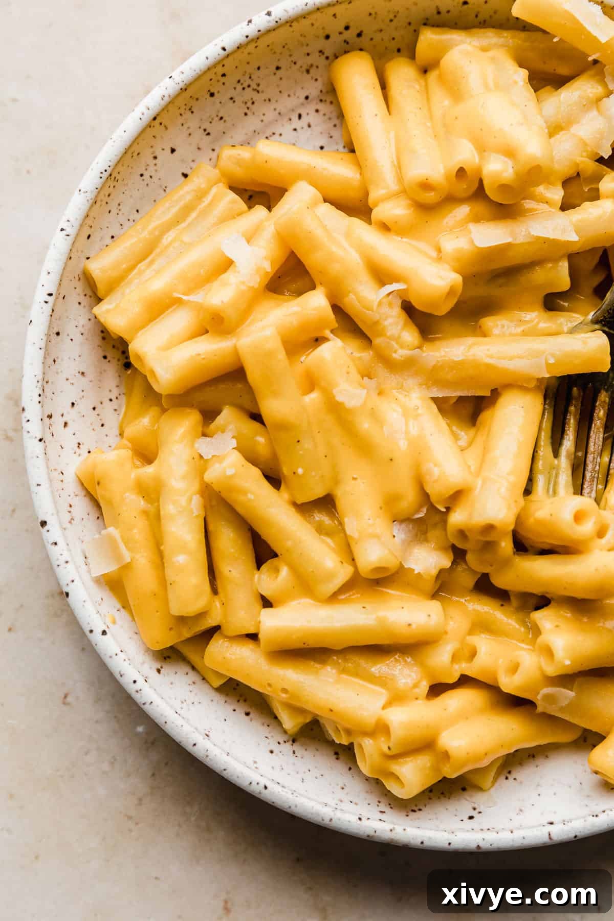 A close-up shot of creamy roasted butternut squash pasta sauce generously coating ziti noodles in a white bowl, ready to be enjoyed.
