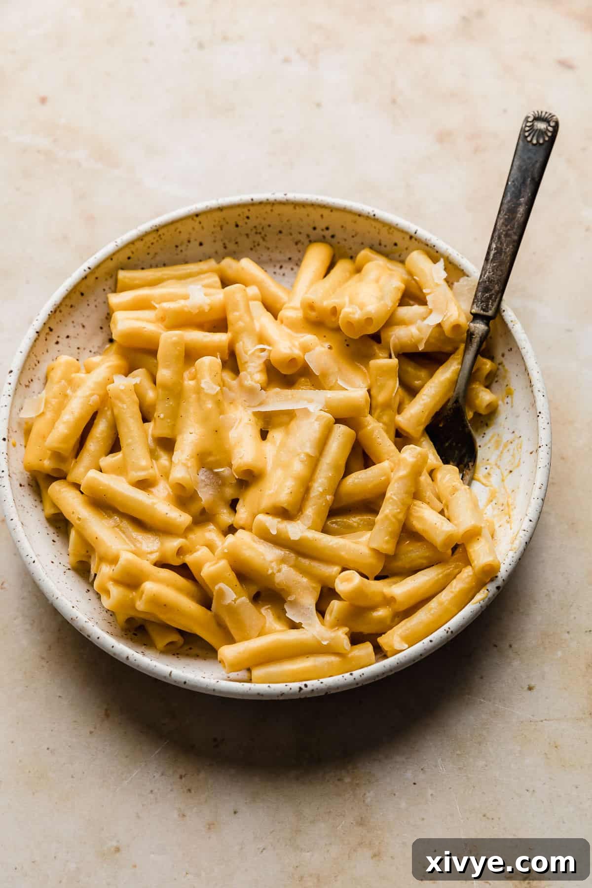 A close-up of a white plate generously filled with ziti noodles coated in a rich, orange butternut squash pasta sauce, ready to be savored.