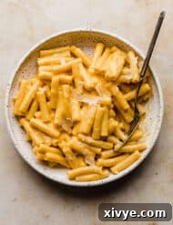 Ziti noodles generously covered in a creamy, vibrant orange butternut squash pasta sauce, served in a white bowl.