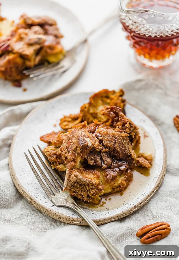 Spiced Pumpkin French Toast Bake 2 Overnight Pumpkin French Toast Casserole on a plate with a fork nearby, drizzled with maple syrup.