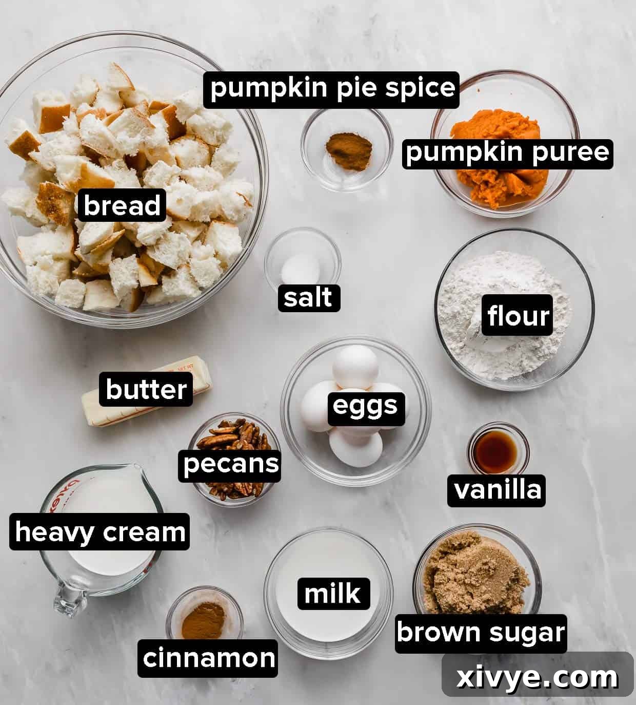 Spiced Pumpkin French Toast Bake 4 Pumpkin French Toast Casserole ingredients laid out in glass bowls on a marble table.