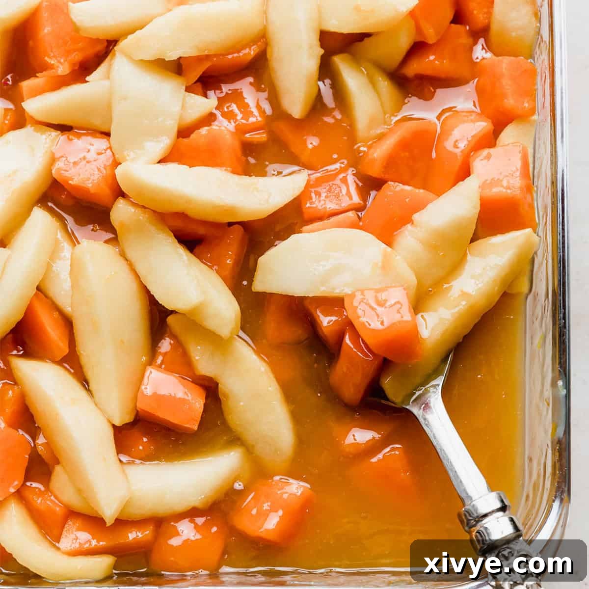 Rich orange juice candied yams, beautifully arranged in a baking dish and generously topped with tender, spiced apples, ready to be served.