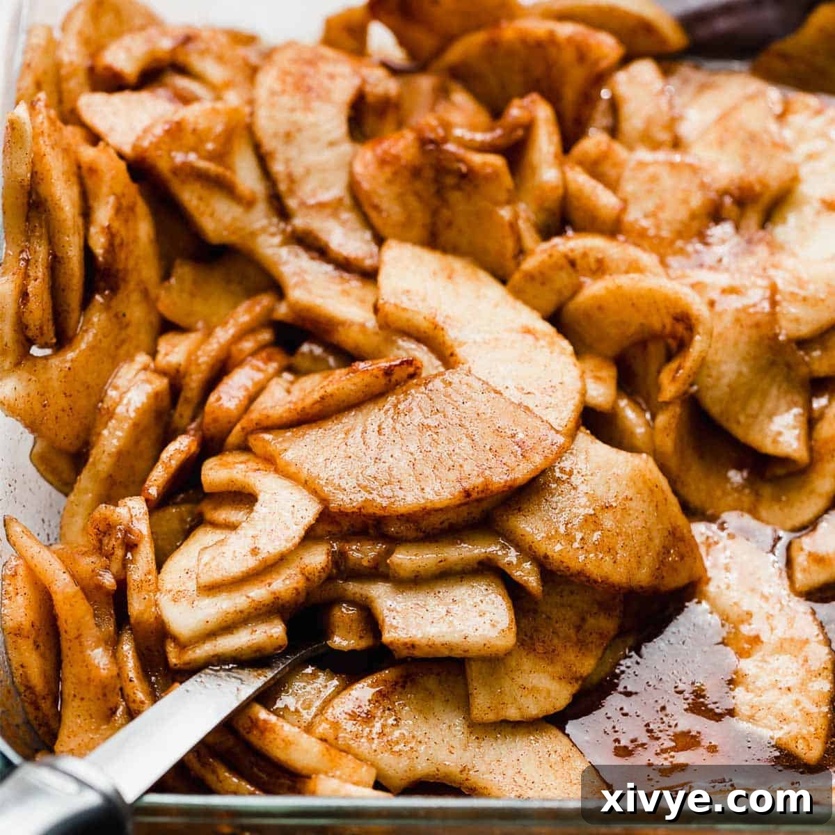 Perfectly baked Cinnamon Baked Apples simmering in a fragrant cinnamon mixture within a clear glass baking pan, showcasing their soft, appealing texture.