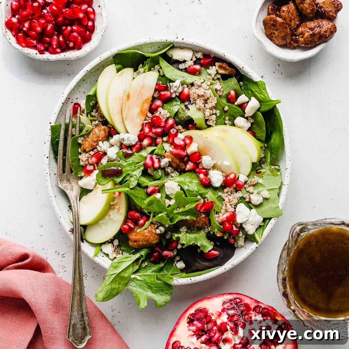 A vibrant Pomegranate Salad generously topped with crisp apples, juicy pomegranate arils, crunchy candied pecans, and delicate gorgonzola cheese, presented on a clean white background.