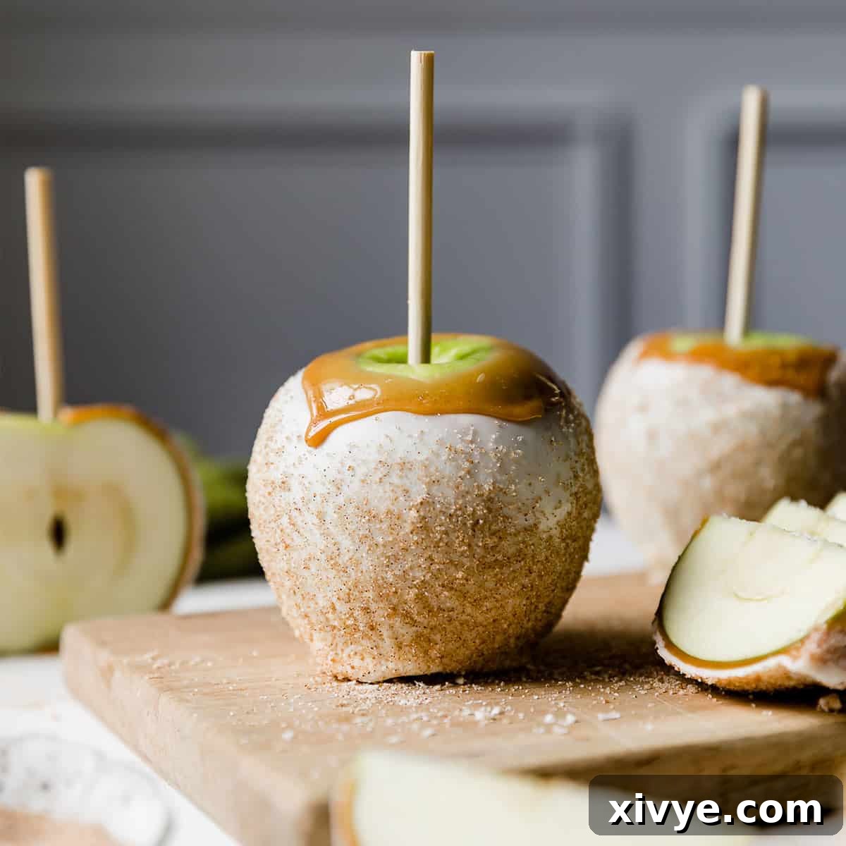 A luscious white chocolate and caramel dipped Rocky Mountain Apple Pie Caramel Apple, artfully presented against a soft light gray background.
