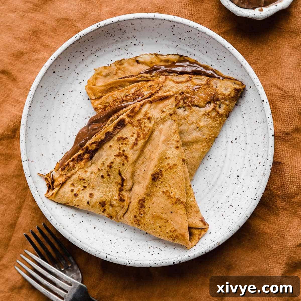 Two delicate Nutella filled pumpkin crepes elegantly arranged on a white plate, inviting a sweet taste of fall.