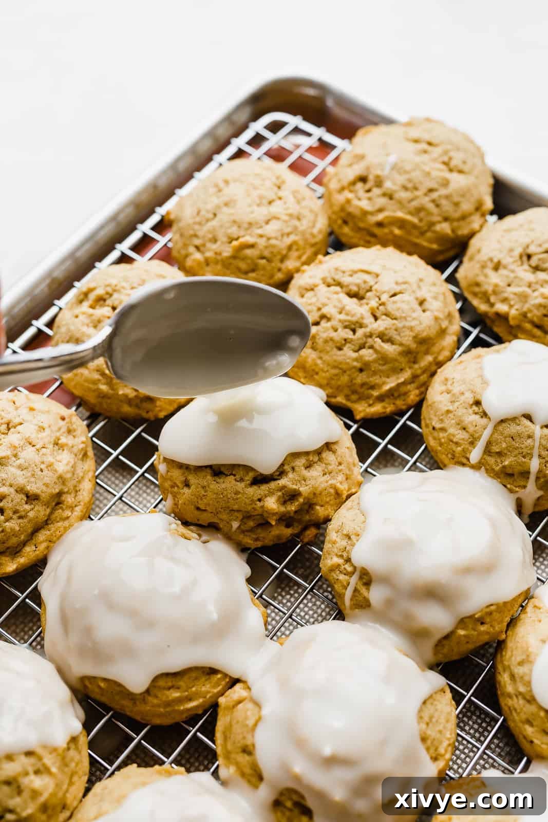 A spoon delicately drizzling glaze over a soft, round pumpkin cookie, enhancing its appeal.