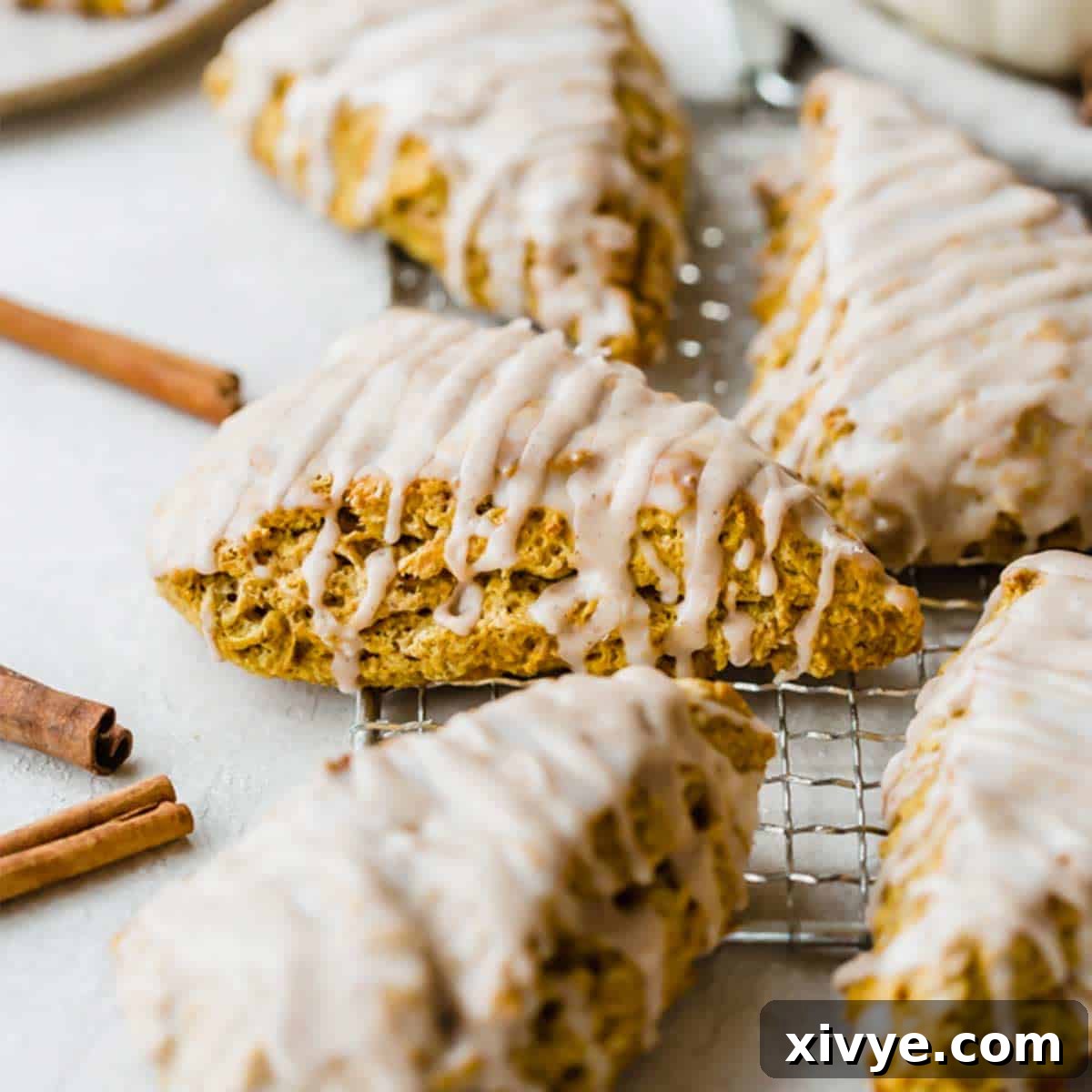A close-up image of a perfectly glazed pumpkin scone on a light gray background, highlighting its tender texture.