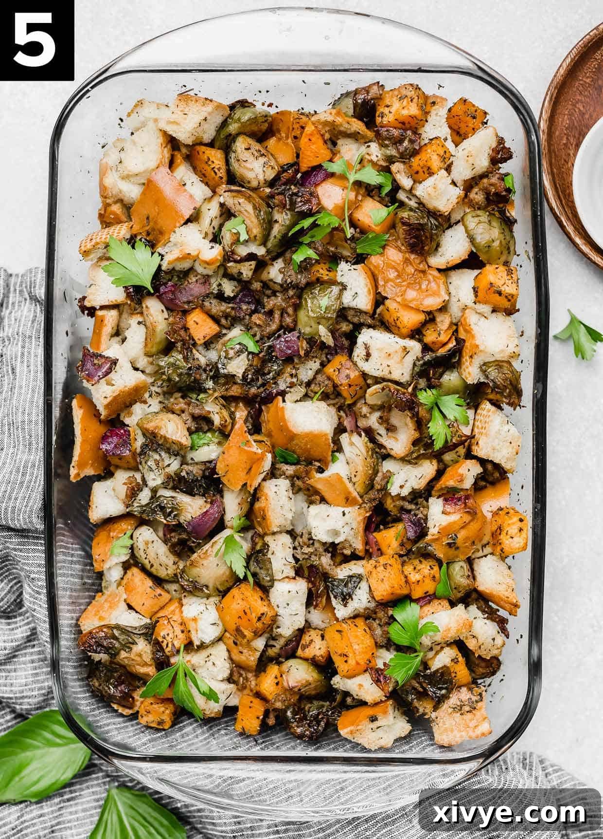 An overhead shot of a glass casserole dish filled with golden-brown Autumn Roasted Vegetable Stuffing, ready to be served, set on a white background.